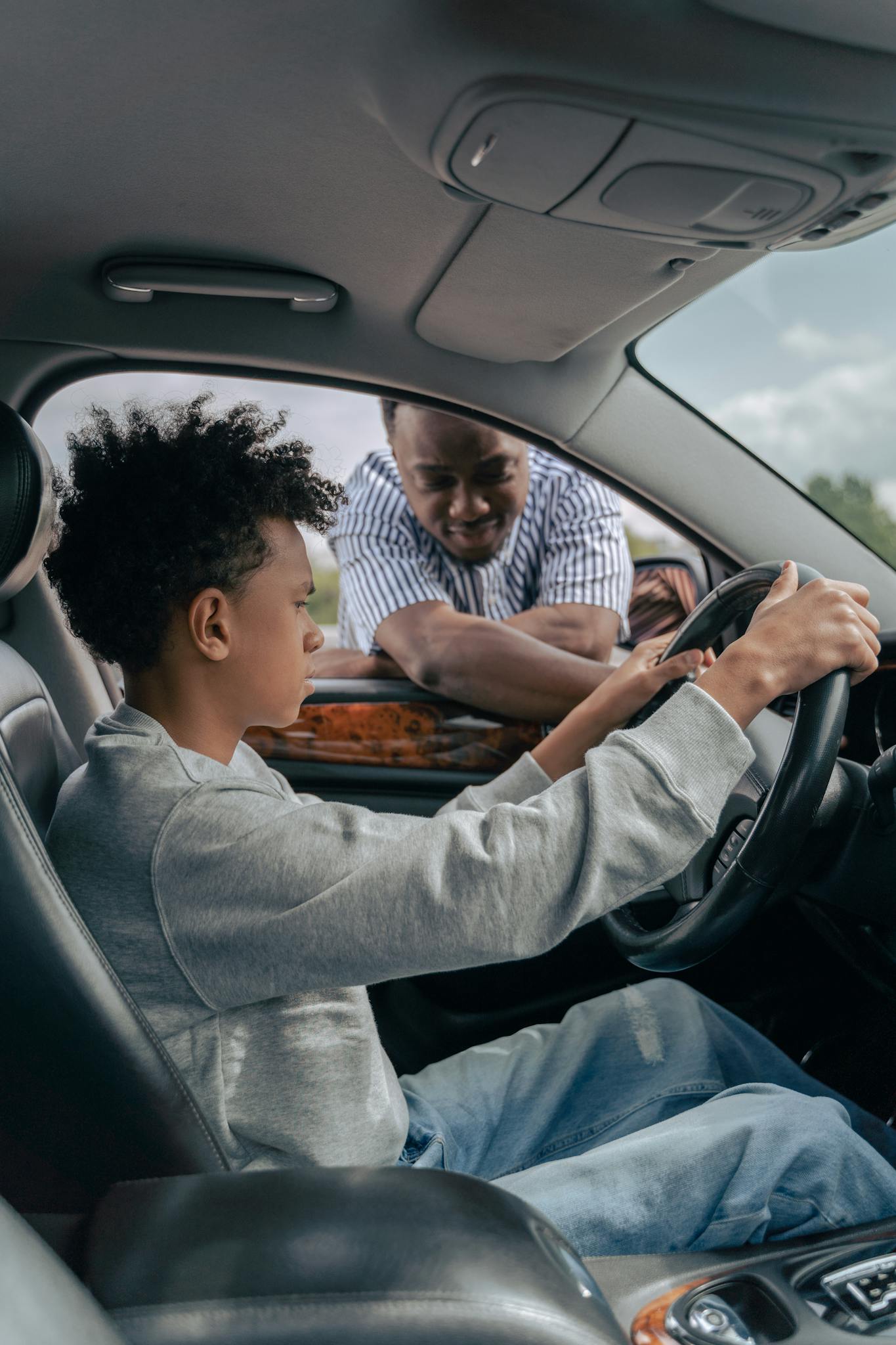A father instructing his son on driving inside a car, focusing on the steering wheel.