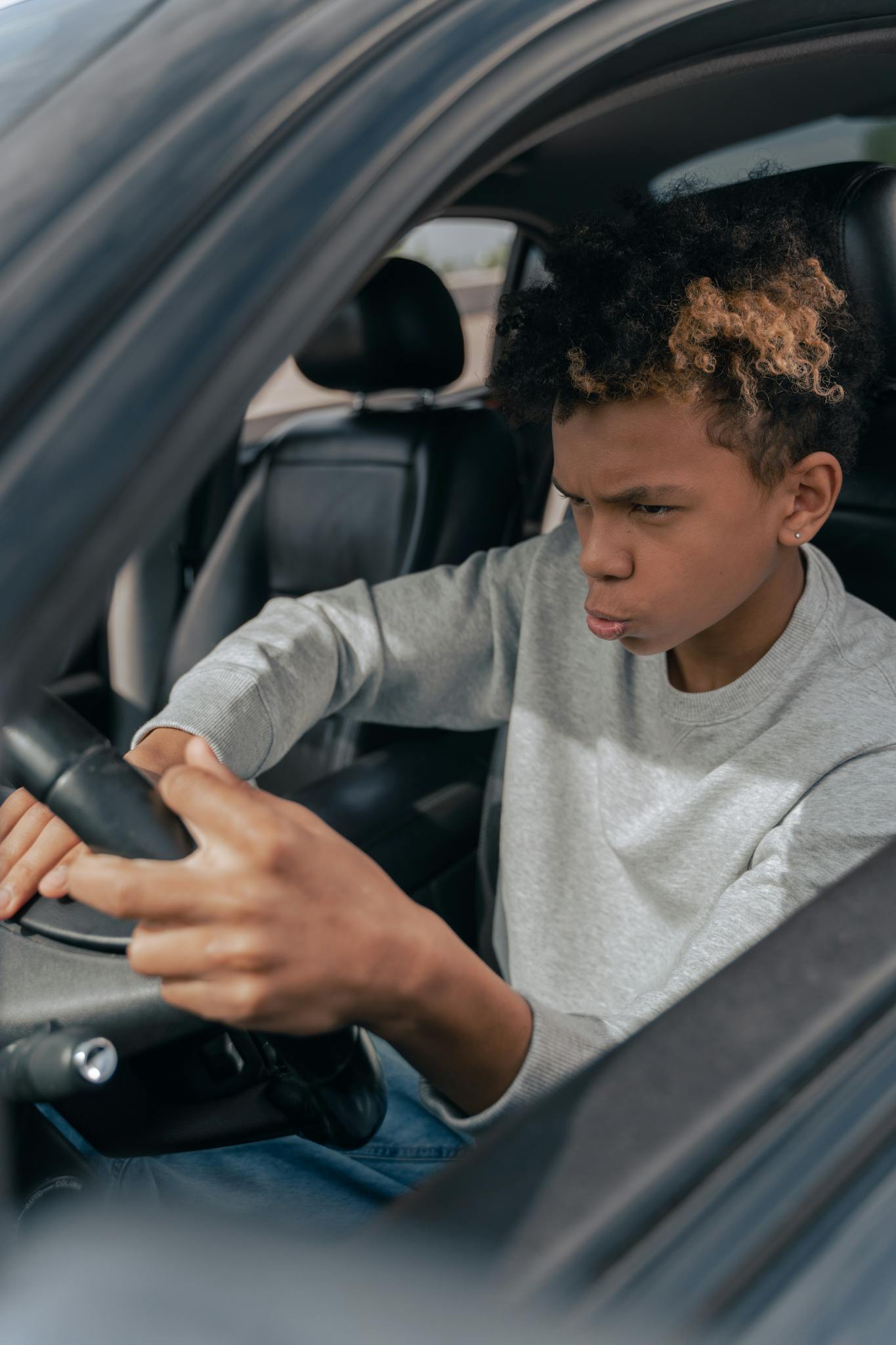 Teenager mimicking driving a parked car indoors with focused expression.